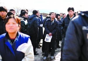 手拿&ldquo;钱少&rdquo;牌子的男子向厂区内张望。昨日，因不满协议离职，400余位松下员工堵在厂门口讨说法。